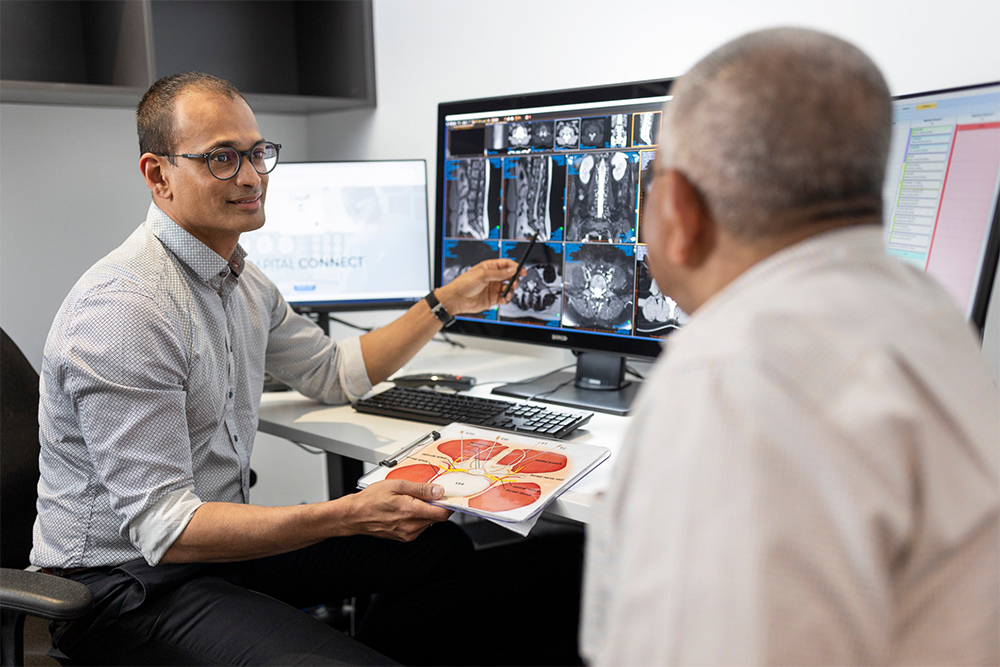 Radiologist talks to patient, showing the findings from their scan on the computer screen.